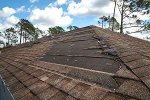 Wind damaged house roof with missing asphalt